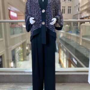 This elegant two-piece set pairs wide-leg trousers with a statement sequin-embellished jacket. The black mesh base creates the perfect canvas for the shimmering overlay, finished with satin lapels and cuffs for a refined contrast. Delicate floral-inspired buttons add a luxe touch, while the relaxed silhouette ensures comfort without compromising on sophistication. Ideal for evening occasions, celebrations, or when you want to shine with understated elegance.  Also available in beige & coffee   Color: black with sequin overlay Details: Wide-leg trousers | Sequin embellished jacket with satin trim & statement buttons Style: Elegant | Modern | Glamorous